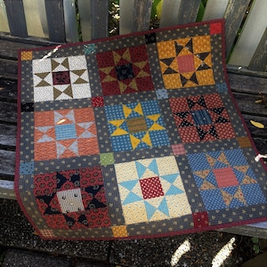 May include: A patchwork quilt with a variety of star patterns in shades of red, blue, yellow, and white. The quilt is made up of nine squares, each with a different star design.