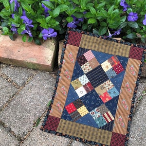 May include: A patchwork quilt with a blue background and a variety of colorful squares. The quilt is surrounded by a brown and black border.