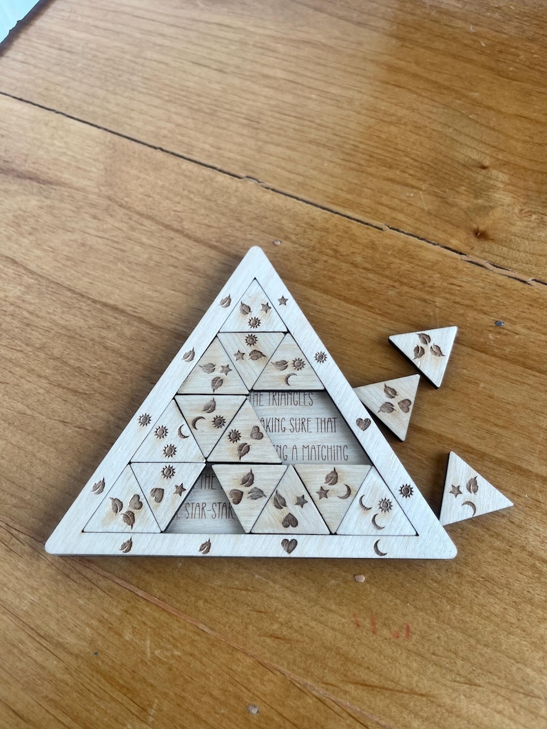 May include: A wooden puzzle in the shape of a large triangle, with smaller triangular pieces. The puzzle has engraved floral and celestial designs. Text on the puzzle reads "THE TRIANGLES MAKING SURE THAT A MATCHING STAR STAR".