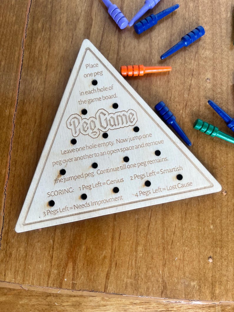 May include: Wooden triangular game board with the text "Peg Game" and instructions for playing. The board has 15 holes and is designed for a peg game.
