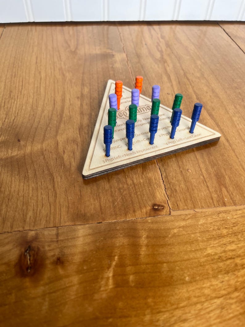 May include: A wooden triangle game board with pegs in various colors, including orange, purple, green, and blue. The board has text that reads "Pegs Left - Needs Improvement" and "Pegs Left - Lost Game".