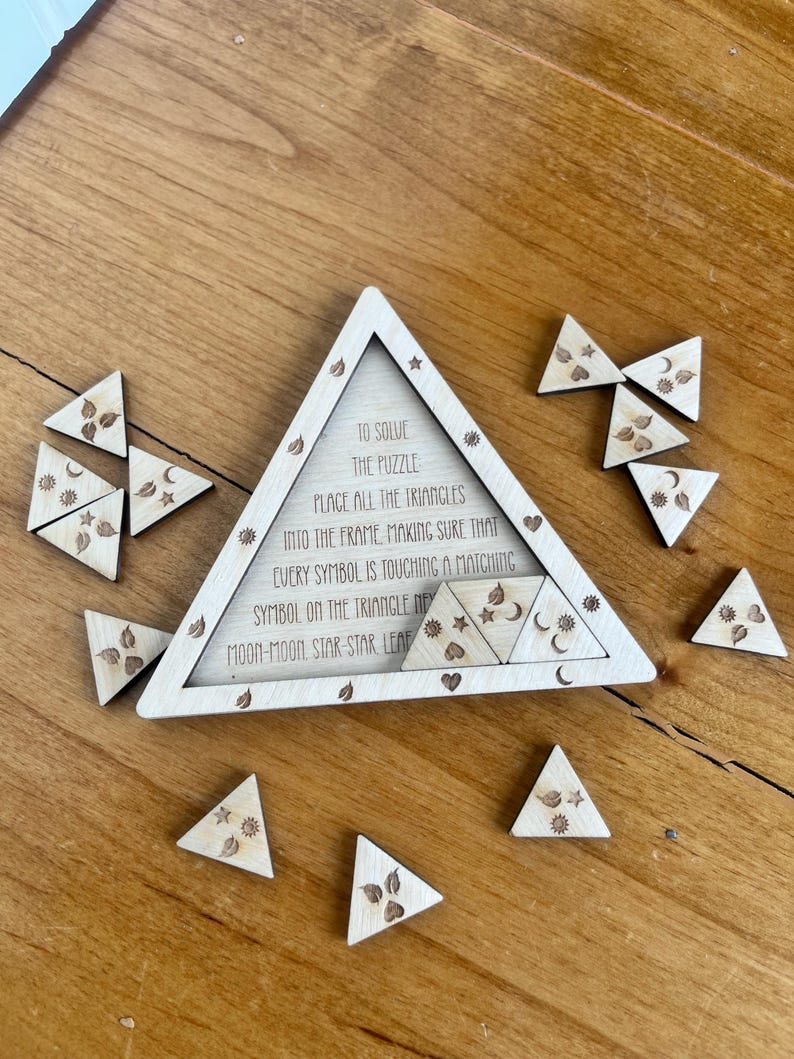 May include: A wooden puzzle with a triangular frame and several smaller triangular pieces. The frame has text that reads "TO SOLVE THE PUZZLE PLACE ALL THE TRIANGLES INTO THE FRAME". The pieces have engraved symbols like stars, moons, and leaves.