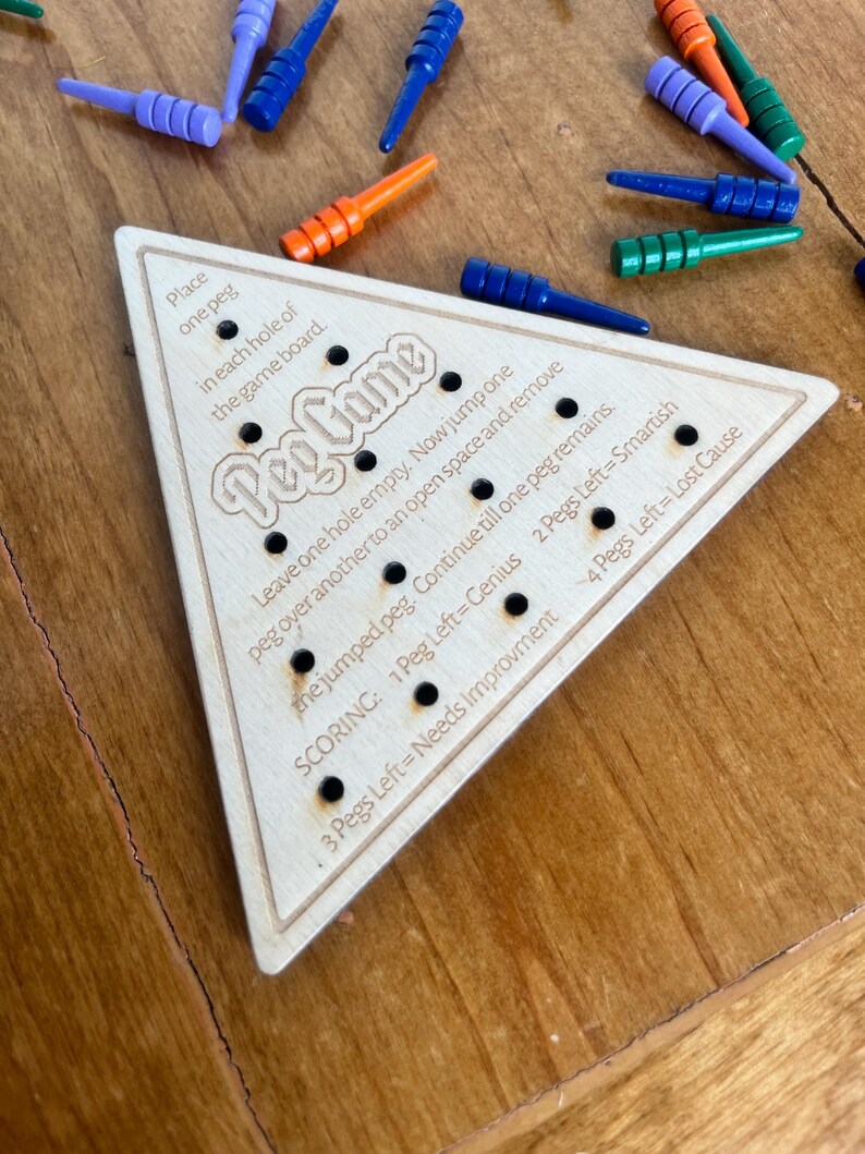 May include: A wooden triangular game board with holes and pegs. The board has the text "Peg Game" and instructions for playing the game. The text on the board reads: "Place one peg in each hole of the game board. Leave one hole empty. Now jump one peg over another to an open space and remove the jumped peg. Continue till one peg remains. SCORING: 1 Peg Left=Genius 2 Pegs Left=Smartish 3 Pegs Left = Needs Improvement 4 Pegs Left=Lost Cause"