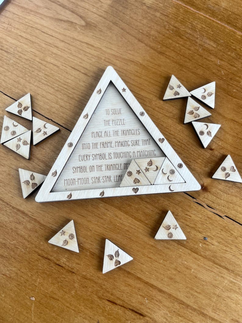 May include: Wooden triangle puzzle with engraved symbols and text. The puzzle includes a triangular frame and several smaller triangular pieces. The text reads, "To solve the puzzle, place all the triangles into the frame..." The symbols include moons, stars, and leaves.