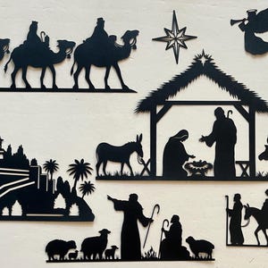 May include: Black silhouette paper cutouts of the nativity scene, including the three wise men, a star, a manger, a donkey, a cow, a sheep, and a church.
