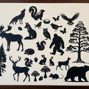 May include: Black silhouette cutouts of various woodland animals, including a moose, deer, bear, fox, squirrel, owl, and more. The cutouts are arranged on a white background.