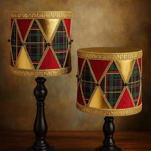 May include: Two decorative drum-shaped lamps with black bases. The lampshades feature a red fabric with gold accents and a green and black plaid pattern. The lamps are on a wooden surface.