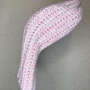 May include: A crocheted golf club head cover, predominantly light pink with white stripes. The cover is designed to protect the head of a golf club. The crochet stitch is clearly visible, showcasing the handmade quality of the item.