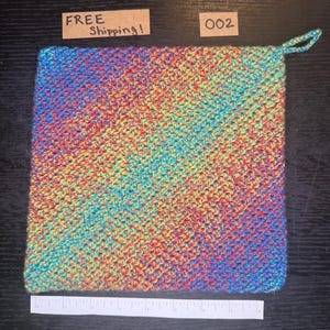 May include: A square, multi-colored crochet potholder with a loop for hanging. The potholder is made with a variety of yarn colors, including red, yellow, blue, and green. The text "002" is visible.