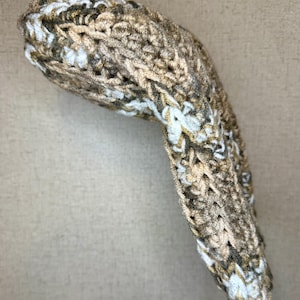 May include: A hand-knitted golf club head cover. The cover is made from a chunky yarn in a mix of brown, beige, and white. The cover is designed to protect the head of a golf club from wear and tear.