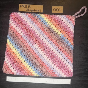 Puede incluir: Un agarrador de ganchillo hecho a mano y colorido con un lazo para colgar. El agarrador presenta un patrón de rayas diagonales en tonos de rosa, rojo, amarillo, azul y marrón. El texto "001" es visible.