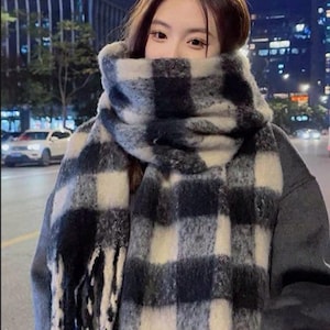 May include: A black and white checkered scarf with fringe. The scarf is made of a soft, fuzzy material.