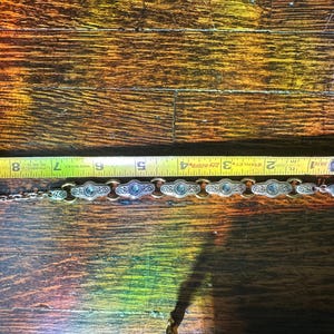 May include: Silver-toned bracelet with oval-shaped links, each featuring a central blue stone. The bracelet is approximately 6 inches long, as measured by a yellow tape measure. The bracelet has a decorative design.