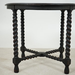 May include: Dark brown antique side table with a round top and four spiral-turned legs. The legs are connected by an X-shaped stretcher near the base. The table is made of wood and has a classic design.