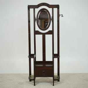 May include: A dark wood hall tree with an oval mirror, a drawer, and two small shelves. The hall tree has a coat hook and two umbrella holders. The design is a classic style.