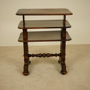May include: A dark brown, three-tiered side table with a rectangular top and shelves. The table has ornate, turned legs and a decorative stretcher. The table is approximately 76 cm tall.