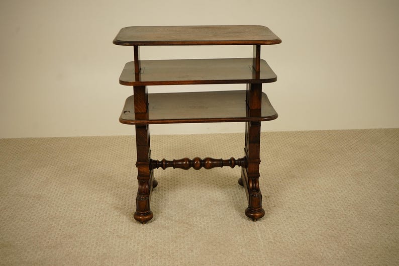May include: A dark brown, three-tiered side table with a rectangular top and shelves. The table has ornate, turned legs and a decorative stretcher. The table is approximately 76 cm tall.
