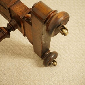 May include: Close-up of a section of a dark brown wooden furniture piece. The piece has ornate, turned legs with brass castors. The wood has a glossy finish, and the design suggests a vintage or antique style.