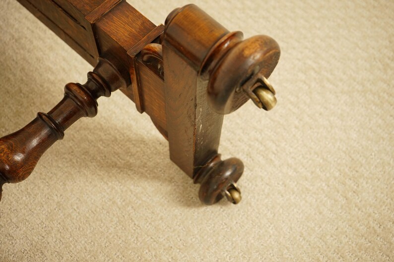 May include: Close-up of a section of a dark brown wooden furniture piece. The piece has ornate, turned legs with brass castors. The wood has a glossy finish, and the design suggests a vintage or antique style.