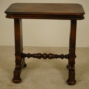 May include: A small, antique wooden side table with a rectangular top and four legs. The table is made of dark brown wood and features decorative carvings on the legs and a stretcher bar. The table is approximately 61 cm tall.