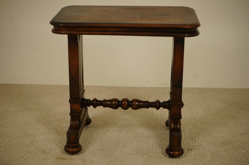 May include: A small, antique wooden side table with a rectangular top and four legs. The table is made of dark brown wood and features decorative carvings on the legs and a stretcher bar. The table is approximately 61 cm tall.