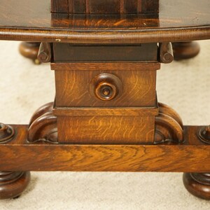 May include: Close-up of a dark brown, antique wooden table base. The table has a round top and a detailed pedestal base with carved accents. The wood grain is visible, and the table appears to be well-preserved.