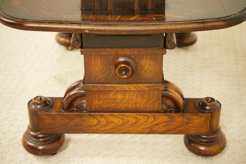 May include: Close-up of a dark brown, antique wooden table base. The table has a round top and a detailed pedestal base with carved accents. The wood grain is visible, and the table appears to be well-preserved.