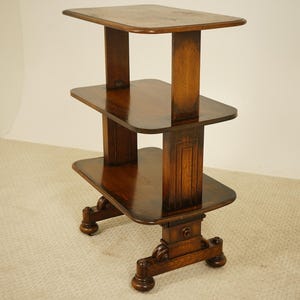 May include: A three-tiered, dark wood side table with a rectangular top and two lower shelves. The table has a decorative base with carved details and is supported by four rounded feet. The wood has a glossy finish.
