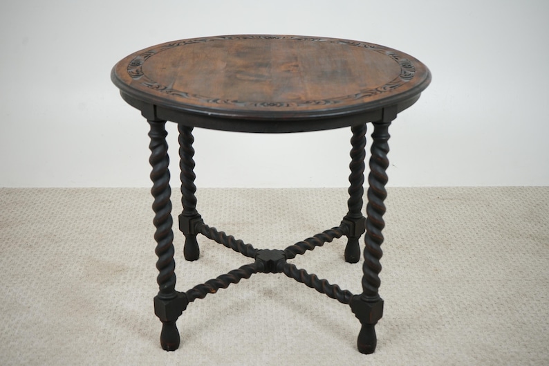 May include: A dark brown, antique side table with a round top and intricately carved edges. The table has four twisted legs and an X-shaped support base. The table is approximately 24 inches tall and 24 inches wide.