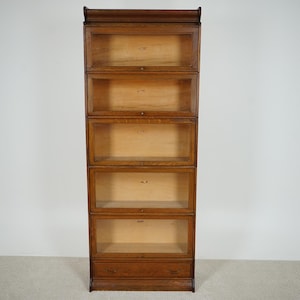 May include: A tall, antique wooden bookcase with five sections, each with a glass door. The bookcase is made of a warm-toned wood and has a classic design, perfect for storing books or displaying items. The bookcase is approximately 72 inches tall.