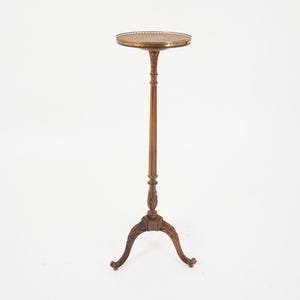 May include: A tall, antique plant stand with a round, ornate top and a slender, wooden stem. The base features a tripod design with curved legs. The stand is made of dark wood and has decorative carvings.