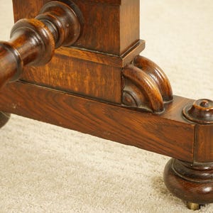May include: Close-up of a dark brown wooden table leg with detailed carvings. The leg has a turned design and a rounded foot with a brass accent. The wood grain is visible, showing the natural texture of the wood.