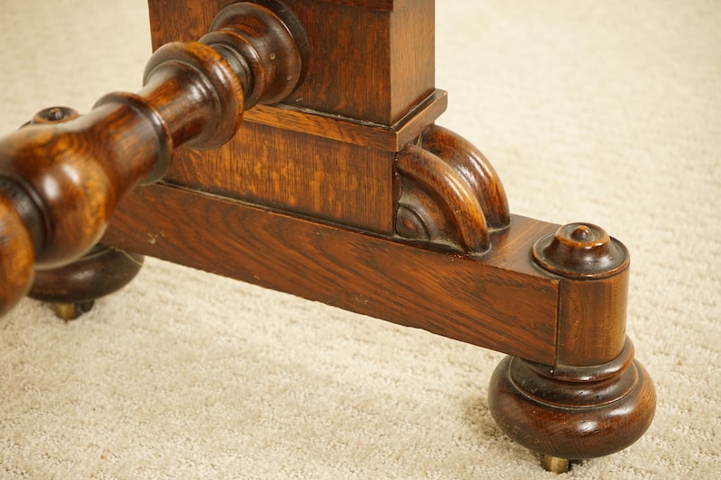 May include: Close-up of a dark brown wooden table leg with detailed carvings. The leg has a turned design and a rounded foot with a brass accent. The wood grain is visible, showing the natural texture of the wood.