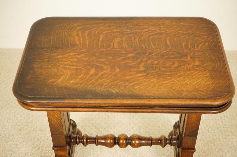 May include: An antique wooden table with a rectangular top and decorative legs. The table is made of dark brown wood with a visible wood grain pattern. The table's top is approximately 61 cm long and 46 cm wide.