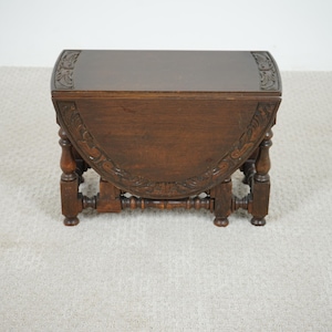 Peut inclure: Petite table en bois antique, finition brun foncé. La table, de forme semi-circulaire, présente des détails sculptés sur les bords et les pieds. Elle mesure environ 61 cm de large et 51 cm de profondeur.