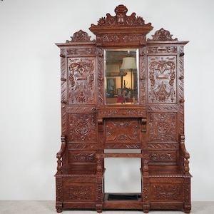 Può includere: Albero da ingresso in legno scuro e ornato con dettagli intagliati, uno specchio centrale e due panche. L'albero da ingresso presenta intricati disegni floreali e a volute ed è un pezzo forte per un ingresso.