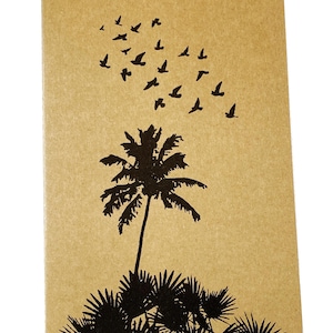 May include: A tan-colored notebook featuring a black silhouette of a palm tree and a flock of birds. The palm tree is at the bottom, with birds flying upwards. The notebook has rounded corners.