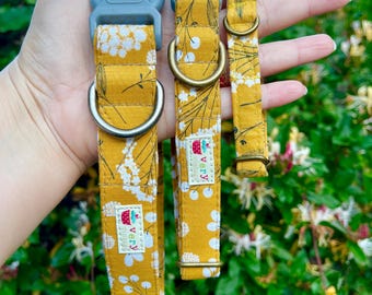 May include: Three yellow dog collars with a white floral pattern. The collars have a gray buckle and a brass D-ring. The collars are labeled "Very" with a cupcake logo.