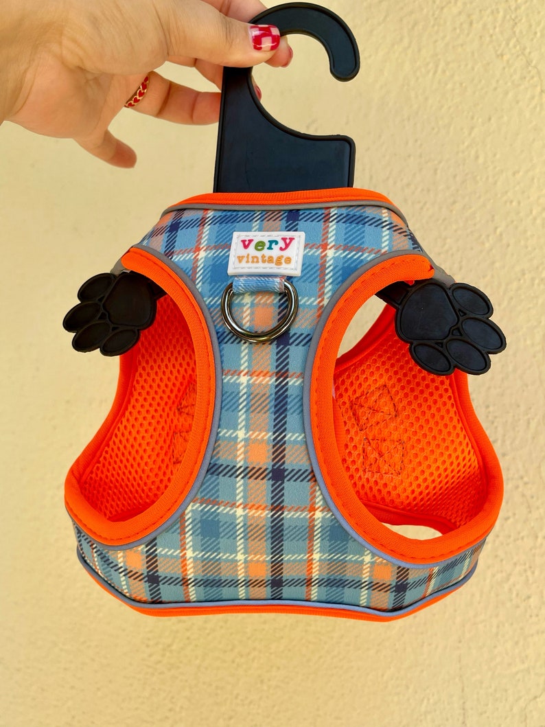 Puede incluir: Arn&eacute;s para perro de cuadros naranja y azul con una huella de pata negra a cada lado. El arn&eacute;s tiene un anillo en D de metal negro y un gancho de pl&aacute;stico negro. El arn&eacute;s tiene el texto "very vintage" en la parte delantera.