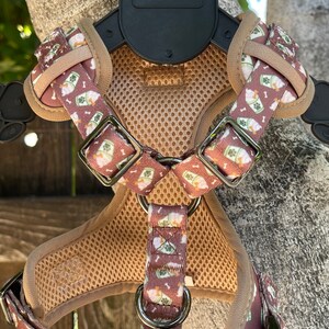 May include: A brown dog harness with a white and green pattern of ice cream cones and bones. The harness has a mesh back panel and a metal buckle.