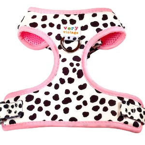 May include: Pink and white dog harness with black spots and a metal ring. The harness has the text "very vintage" on it.