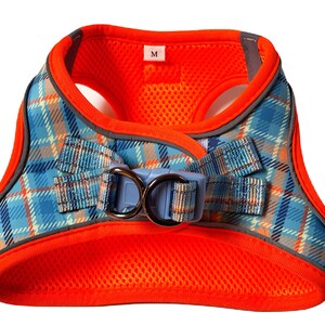 Puede incluir: Arn&eacute;s para perro de cuadros naranja y azul con hebilla azul y plateada. El arn&eacute;s tiene un forro de malla y una etiqueta de talla que dice "M".