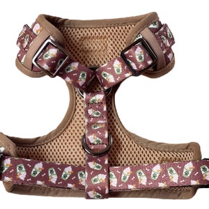 May include: A brown dog harness with a pink and green pattern of ice cream cones and bones. The harness has a mesh lining and adjustable straps.