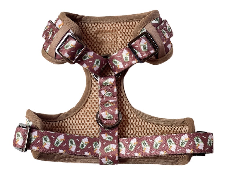 May include: A brown dog harness with a pink and green pattern of ice cream cones and bones. The harness has a mesh lining and adjustable straps.