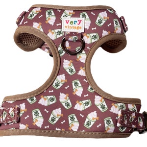 May include: A brown dog harness with a pattern of ice cream cups and bones. The harness has a brown adjustable strap and a metal D-ring. The text "very vintage" is printed on the harness.