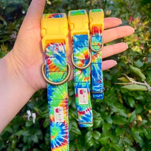 May include: Three tie-dye dog collars with yellow plastic buckles. The collars are in different sizes and feature a rainbow tie-dye pattern with a small strawberry logo.