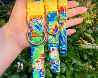 May include: Three tie-dye dog collars with yellow plastic buckles. The collars are in different sizes and feature a rainbow tie-dye pattern with a small strawberry logo.
