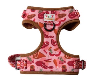 May include: Pink dog harness with a brown trim and a pattern of various meats, including bacon, sausage, and steak. The harness has a metal D-ring and a label that reads "very vintage".
