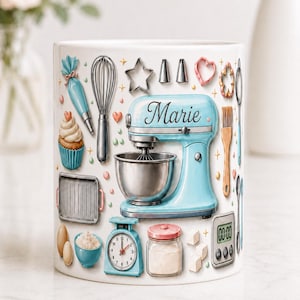 Op de afbeelding: Een witte keramische mok met een lichtblauwe keukenmixer met de naam Marie erop, omringd door illustraties van bakgereedschap zoals een garde, spuitzak, cupcake, weegschaal, kookwekker, bakkwast en diverse uitsteekvormpjes voor koekjes.