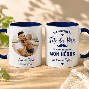 Peut inclure: Deux tasses en céramique blanche avec intérieur et anse bleu foncé. L'une présente une photo circulaire d'un parent et d'un enfant, le texte "Léa et Papa" et "16/06/2026". L'autre affiche "MA PREMIÈRE Fête des Pères ET POUR TOUJOURS MON HÉROS Je t'aime Papa !" avec une icône de moustache bleue.